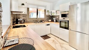 Una cocina moderna con armarios blancos, un refrigerador de acero inoxidable, horno empotrado y una pared decorativa de piedra.