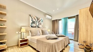 Una habitación de hotel moderna con una cama grande, mesitas de noche, aire acondicionado de pared y vistas al exterior.