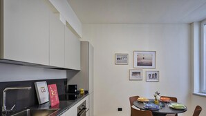 A modern kitchen with white cabinets, a black countertop, and a dining area with a round table and chairs. There are framed pictures on the wall and a window providing natural light.