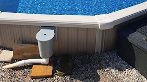 A rectangular hot tub with a clear blue pool, surrounded by gravel and wooden decking.