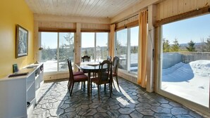 A sunroom with a stone floor, wooden ceiling, and large windows offering a view of a snowy landscape.