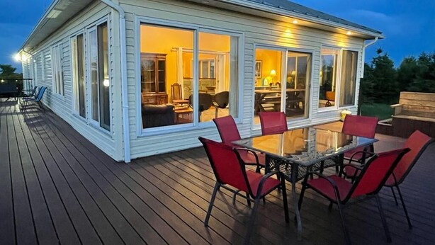 A covered outdoor deck with a glass enclosure, red chairs, and a table.