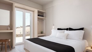 A bedroom with a bed, a desk, and a sliding door to an outdoor area. - Kythea Suites Kythnos (Kithnos)