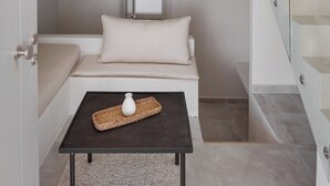A modern interior with a glass staircase, a sofa with a pillow, a small table with a vase, and a ceiling light fixture. - Kythea Suites Kythnos (Kithnos)
