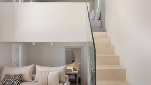 A bedroom with a bed, pillows, a glass railing, and a staircase leading to an upper level. - Kythea Suites Kythnos (Kithnos)