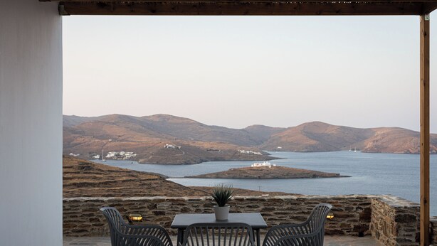 A terrace with a table and chairs overlooking a coastal landscape with hills and a body of water. - Kythea Suites Kythnos (Kithnos)
