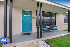 Ein modernes Gebäude mit einer blauen Tür, zwei Gartenstühlen und einer kleinen Terrasse.