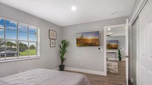 A bedroom with a bed, a window with blinds, a potted plant, and a painting on the wall. - Modern getaway near the beach with room for a boat (West Palm Beach)