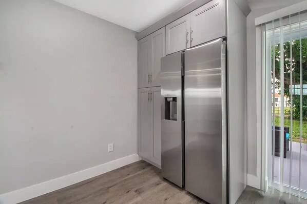A kitchen with white cabinets, a stainless steel refrigerator, and a sliding glass door to the outside. - Modern getaway near the beach with room for a boat (West Palm Beach)