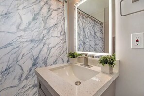 Ein Badezimmer mit Marmor-Spritzschutz, einem Waschbecken mit modernem Wasserhahn und zwei Blumentöpfen.