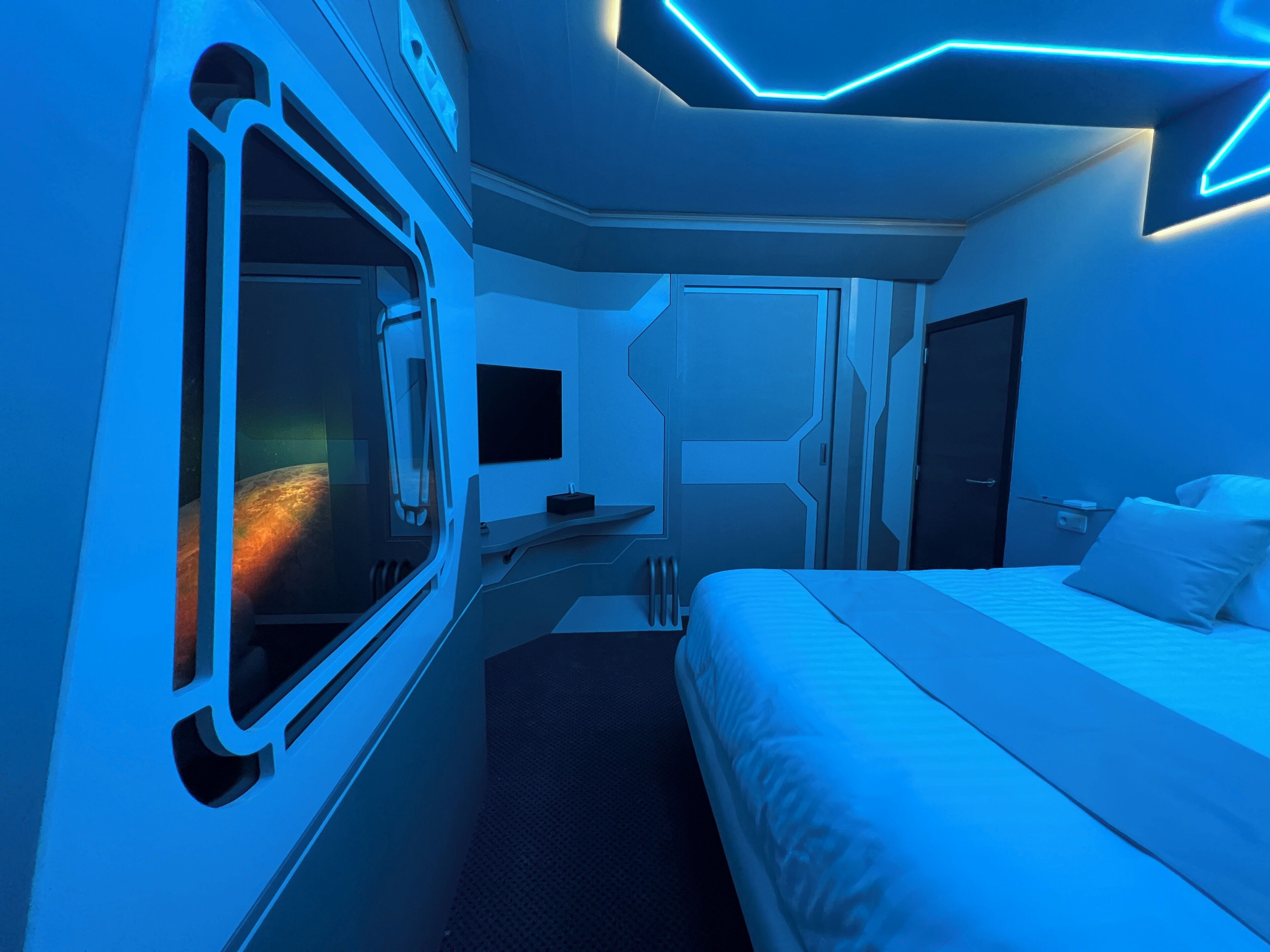 A modern, compact room with a bed, a small bedside table, and a window.