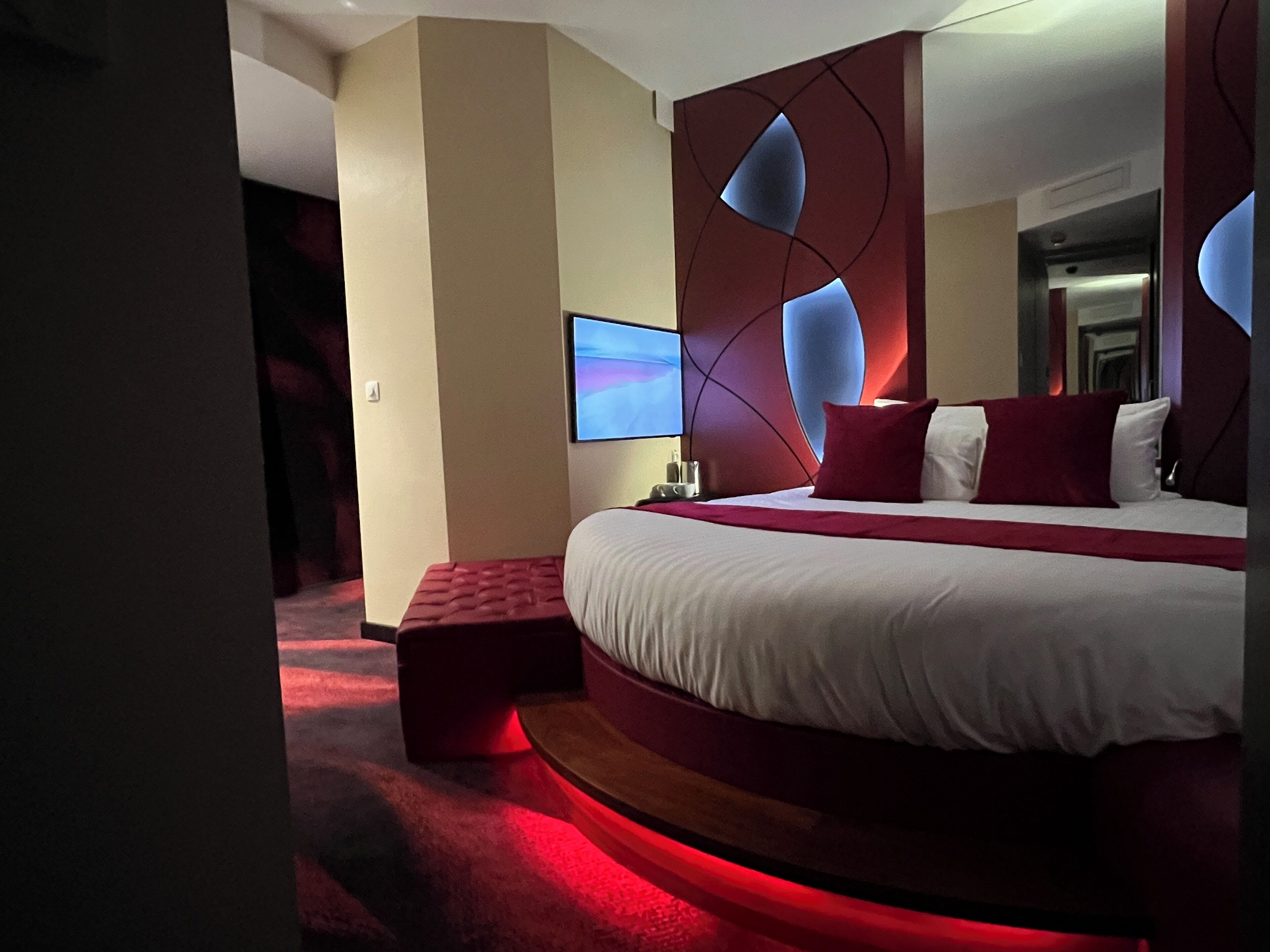 A modern hotel room with a large bed, a flat-screen TV, and a red accent wall.