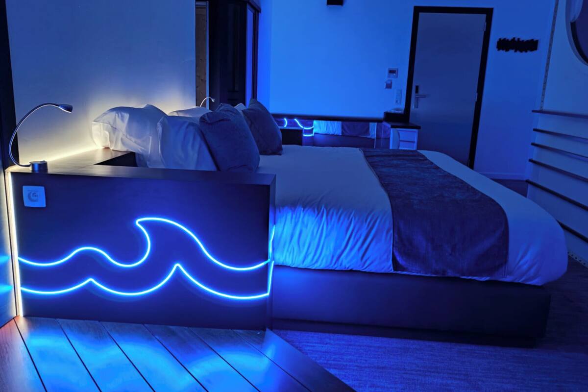 Ein modernes Schlafzimmer mit einem Bett, Nachttischen, einer Lampe und einer Neon-Wellenleuchte.
