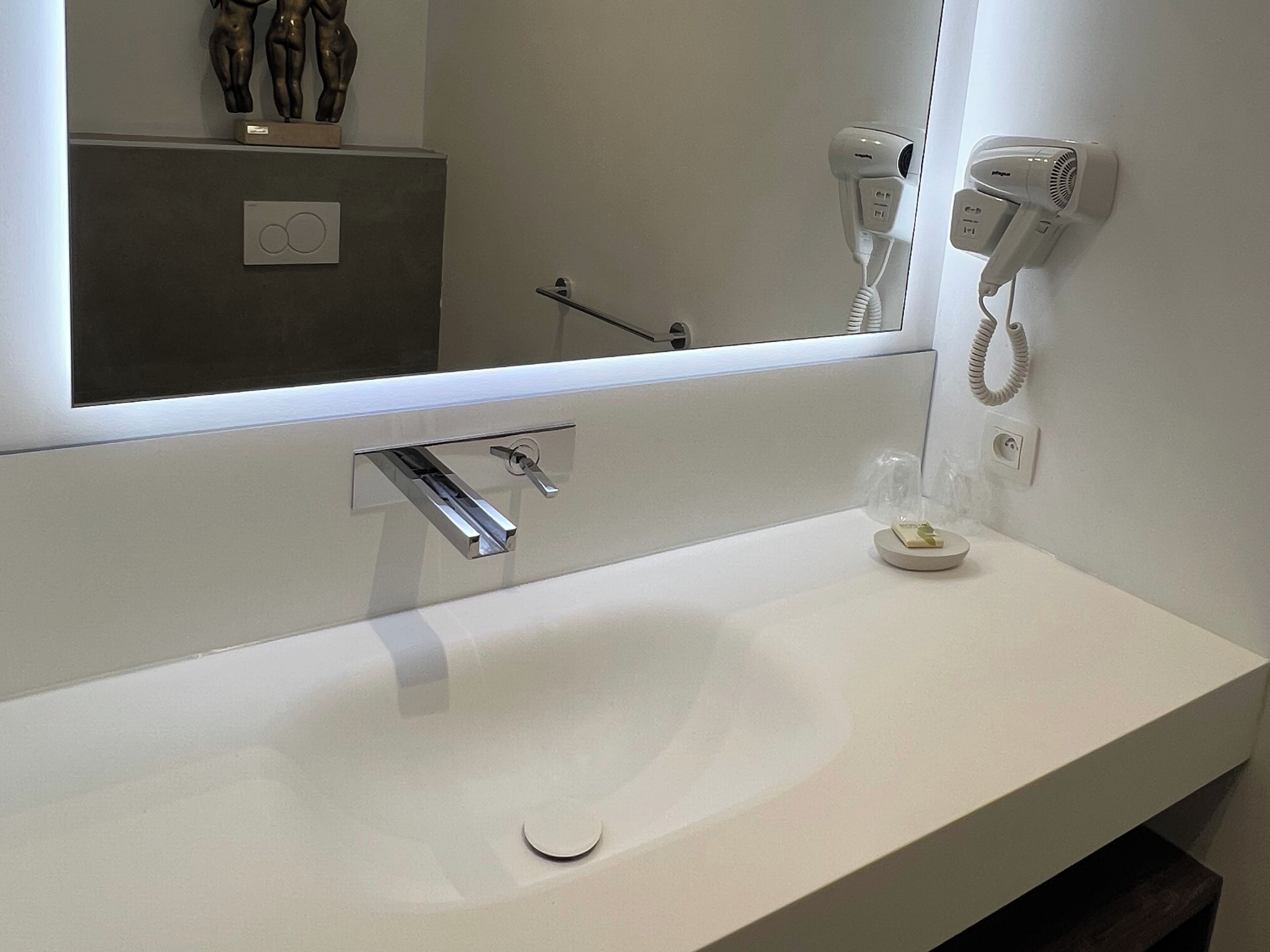 A modern bathroom with a large mirror, a white sink, and two hair dryers mounted on the wall.