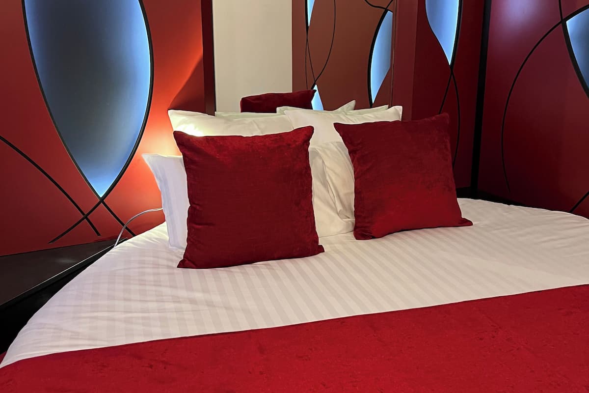 Ein Bett mit rot-weißer Bettwäsche, einer roten Tagesdecke und einem modernen Kopfteil mit abstrakten Mustern.