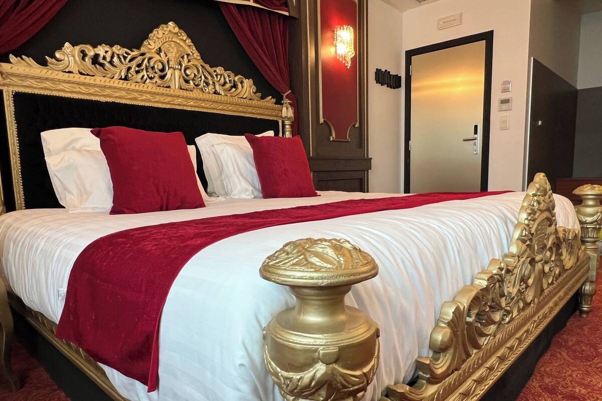 Ein luxuriöses Bett mit goldenem Kopfteil, weißer und roter Bettwäsche und einer roten Tagesdecke.