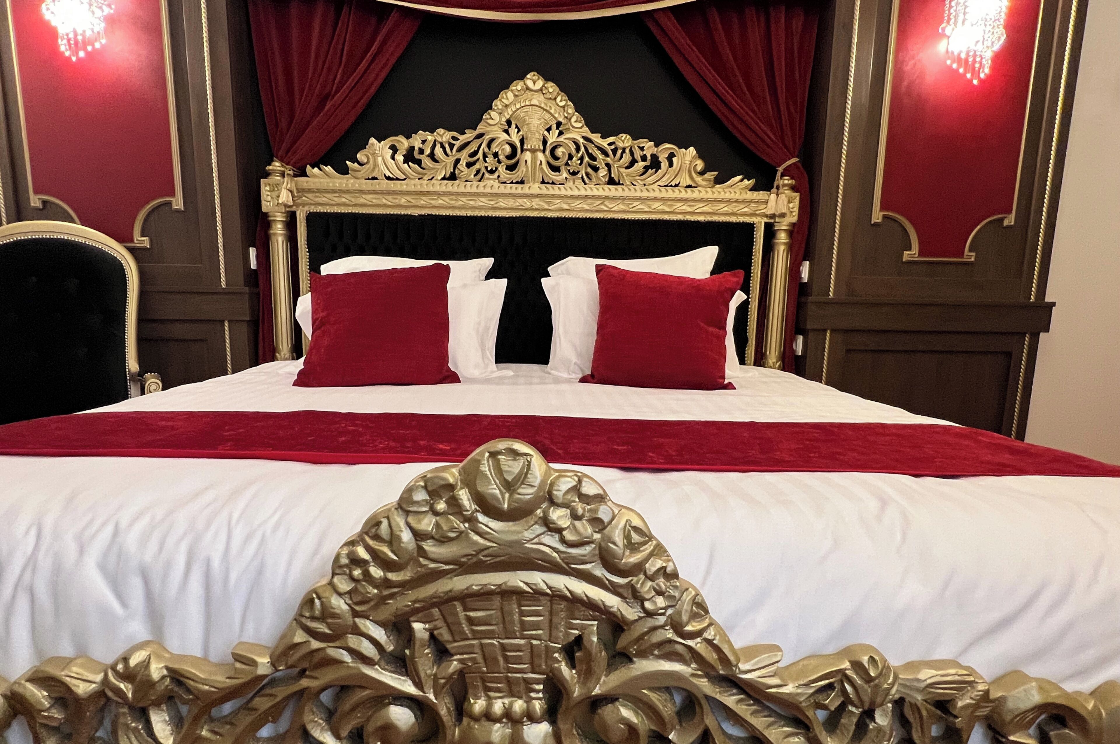 A luxurious bed with ornate gold detailing, red and white bedding, and red curtains.
