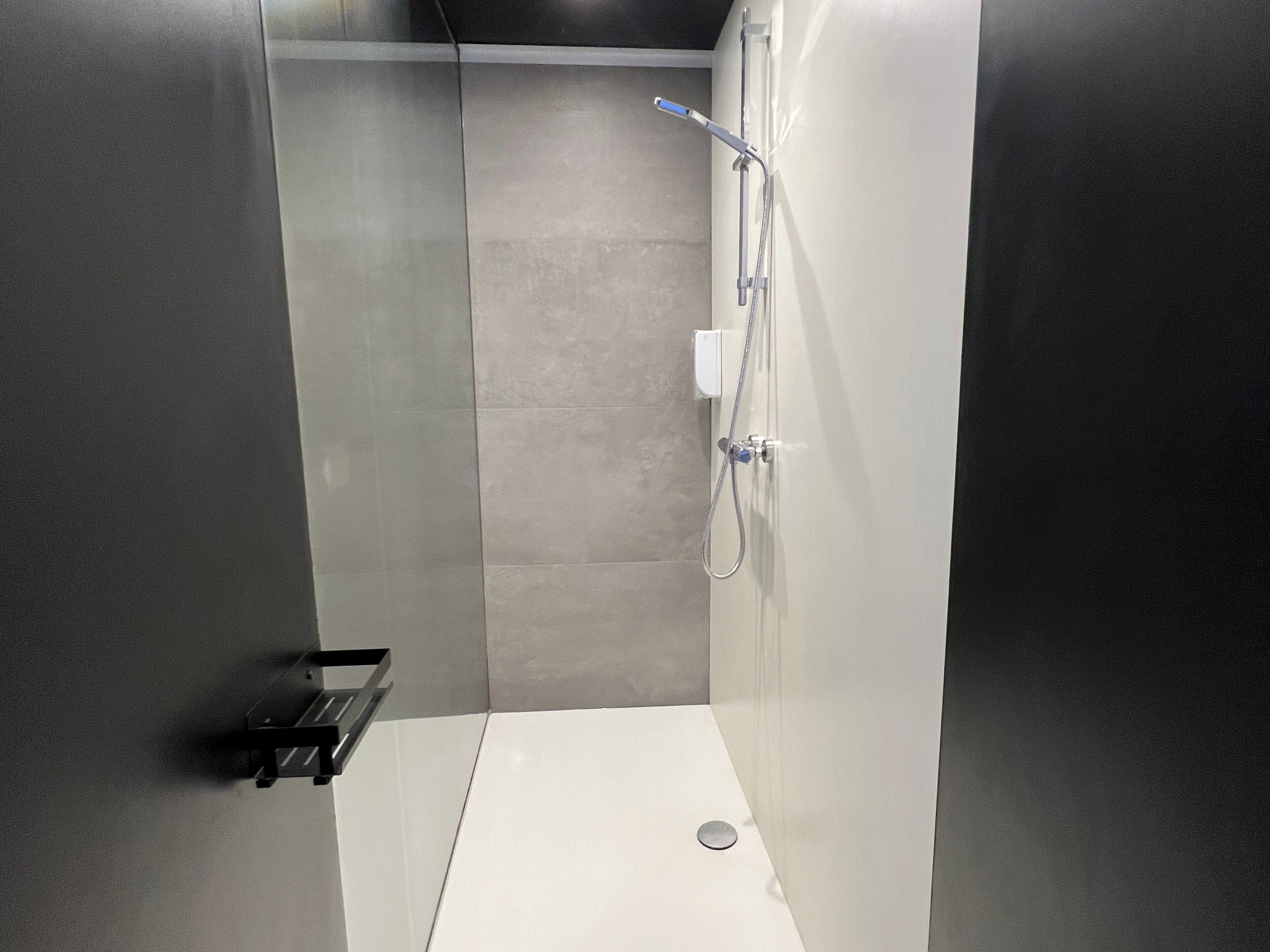 A modern shower with a handheld showerhead, a wall-mounted faucet, and a small shelf.