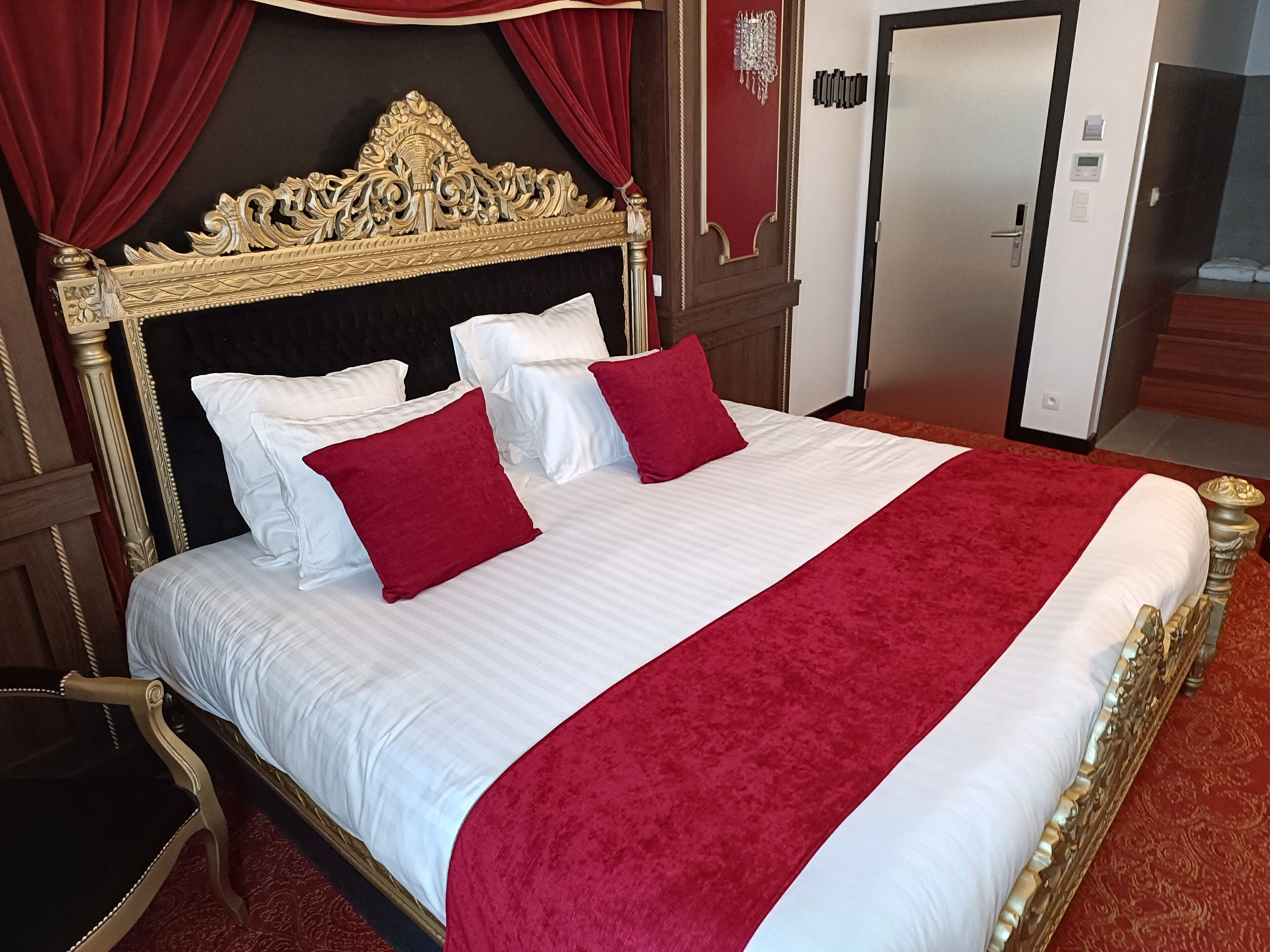 Una habitación de hotel con una cama grande, cortinas rojas y un cabecero clásico y ornamentado.