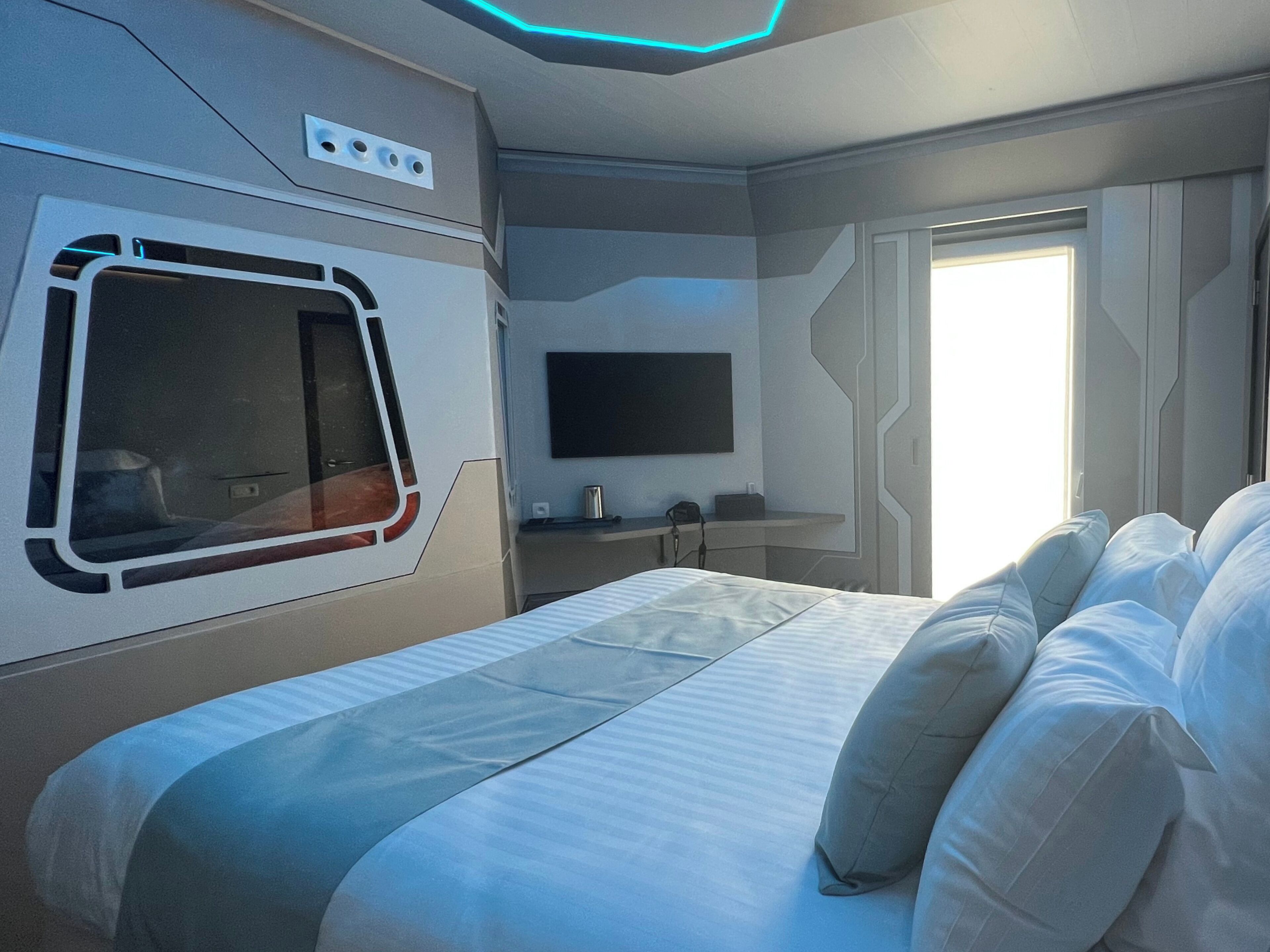 A modern hotel room with a large bed, a TV mounted on the wall, and a window providing natural light.