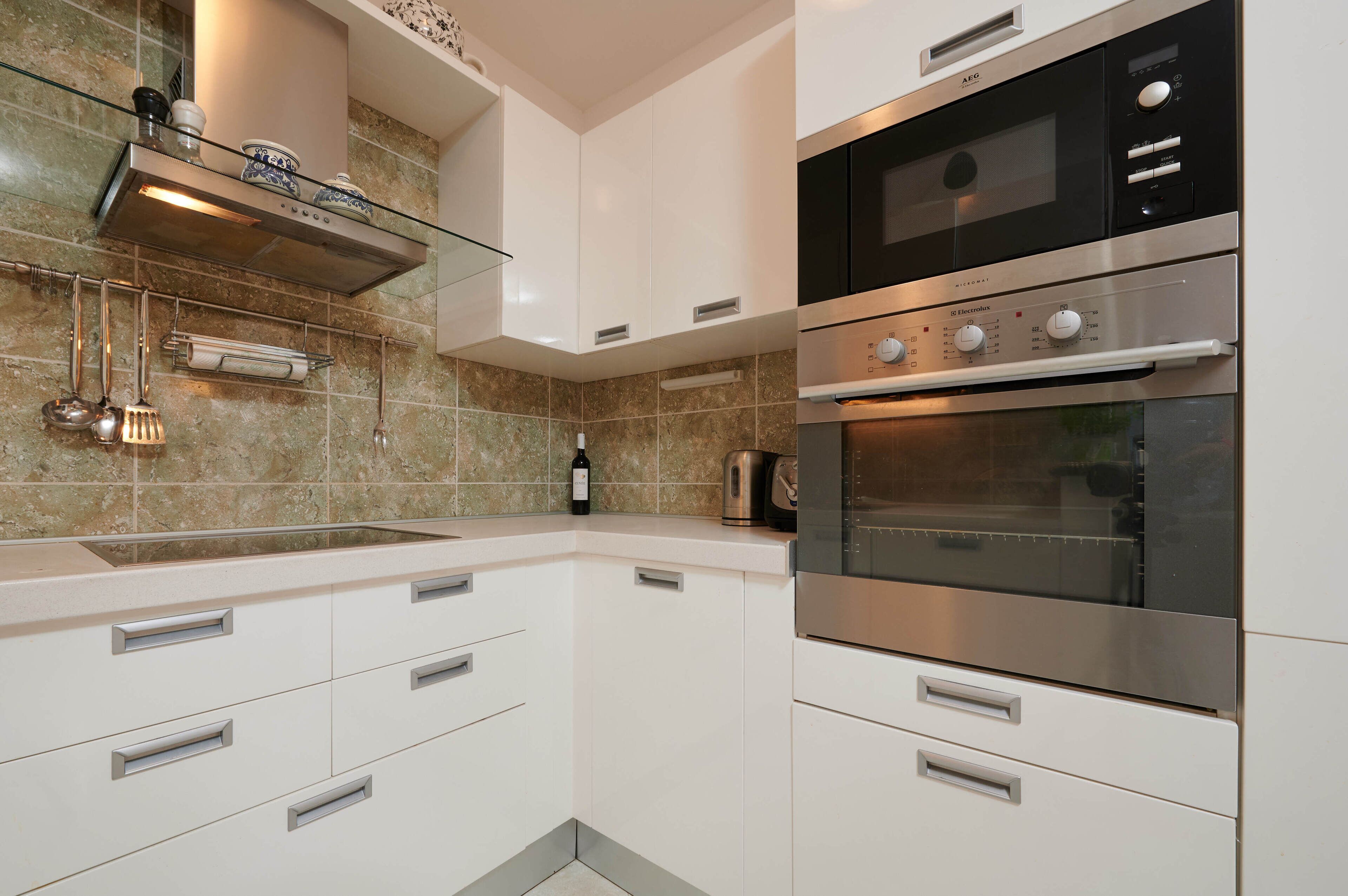 Una cocina moderna con armarios blancos, horno de acero inoxidable y un salpicadero de baldosas color beige.