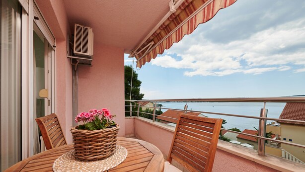 Een balkon met een ronde houten tafel, een rieten mand met bloemen en uitzicht op de zee.