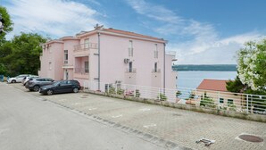Een roze gebouw met een betegeld dak, een parkeerplaats met auto's en een waterpartij op de achtergrond.
