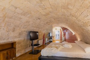 A room with a stone vaulted ceiling, a bed with white linens, a flat-screen TV, and a wooden cabinet.