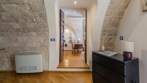 Un pasillo con paredes de piedra, suelo de madera, un radiador blanco y un armario negro con una revista.
