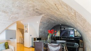 Un interior moderno con un arco de piedra que conduce a un comedor, un televisor de pantalla plana y un jarrón con flores rojas.
