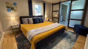 A modern bedroom with a large bed, bedside tables, a rug, and a sliding glass door leading to a balcony.