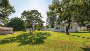 A residential property with a well-maintained lawn, a small detached house, and a fenced yard.