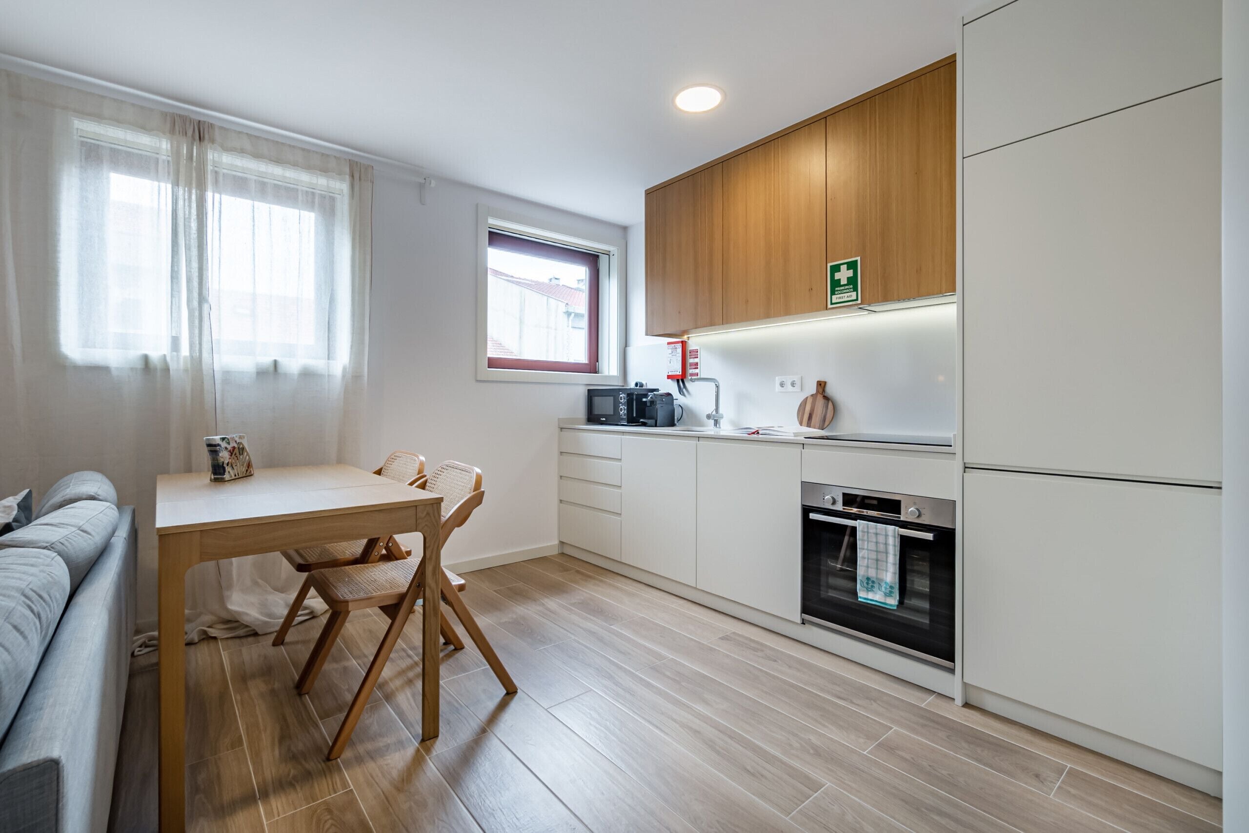 A modern kitchen with wooden cabinets, a built-in oven, and a dining area with a table and chairs.