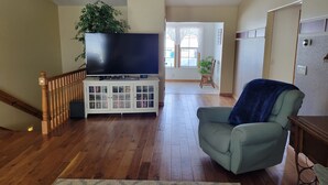 Un soggiorno con una TV su un mobile bianco, una poltrona verde, pavimento in legno e una scala.