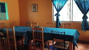 Un comedor con una mesa larga y sillas, una ventana con cortinas, y un cuadro colgado en la pared.