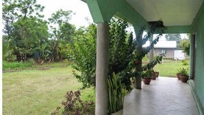 Un espacio exterior cubierto con piso de baldosas, plantas en macetas y vista a un jardín con árboles.