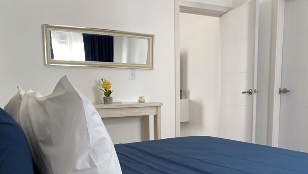 Ein Hotelzimmer mit Bett, Nachttisch mit Blumenvase, Spiegel und Tür.