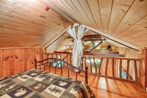 Quarto de cabana de madeira com cama, teto de madeira e escada para um andar superior.