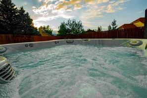 Un jacuzzi rodeado por una valla de madera y árboles, con un atardecer de fondo.