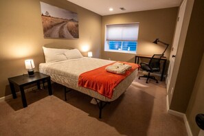 Un dormitorio con una cama, dos mesitas de noche con lámparas, un escritorio con silla, una ventana con persianas y un cuadro en la pared.