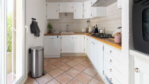 A compact kitchen with white cabinets, a tiled floor, a stainless steel trash bin, and a window providing natural light. - Jolie Villa Liwa Entièrement Rénovée Avec Piscine - 8 Pers (Velaux)
