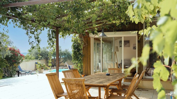 An outdoor patio with a wooden table and chairs, surrounded by potted plants and a view of the sea. - Jolie Villa Liwa Entièrement Rénovée Avec Piscine - 8 Pers (Velaux)