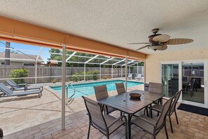 Un patio cubierto con piscina, mobiliario exterior y ventilador de techo.
