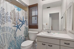 Un baño con cortina de ducha con diseño de coral y estrellas de mar, un inodoro, un lavabo con artículos de tocador y un espejo sobre el lavabo.