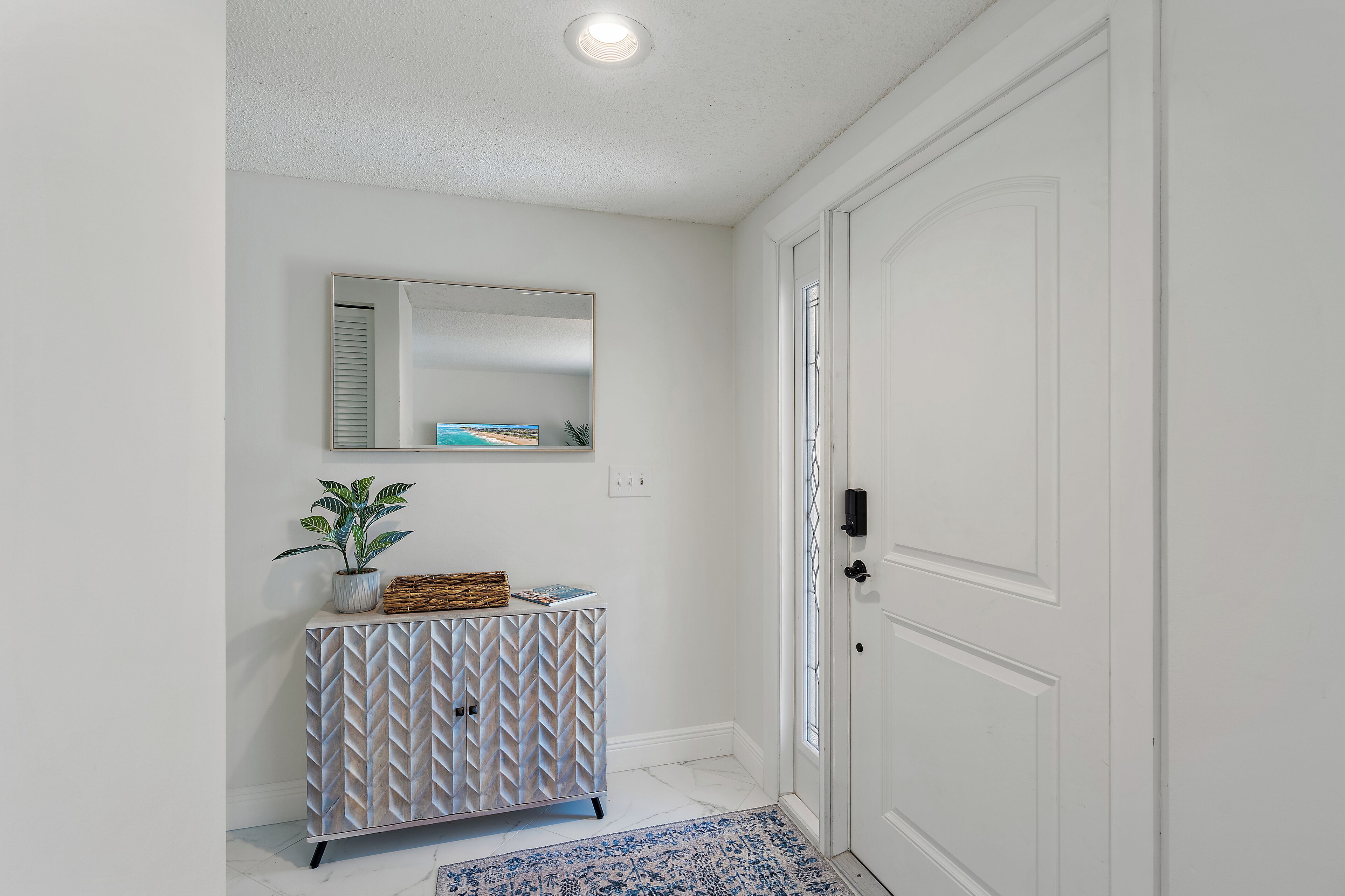 A hallway with a white door, a mirrored wall, and a patterned cabinet.