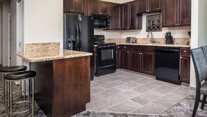 A modern kitchen with dark wood cabinets, granite countertops, a black refrigerator, a microwave, a stove, and a dishwasher.
