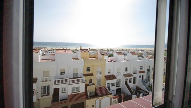 A view from a window overlooking a coastal town with terracotta-roofed buildings and a beach in the distance.