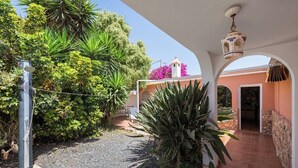 A covered outdoor area with a gravel path, surrounded by lush greenery and a building with a pink facade. - Home2Book Quiet Villa with Private Pool (Triquivijate)