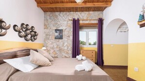 A bedroom with a stone wall, wooden ceiling, and a bed with beige bedding. - Home2Book Quiet Villa with Private Pool (Triquivijate)