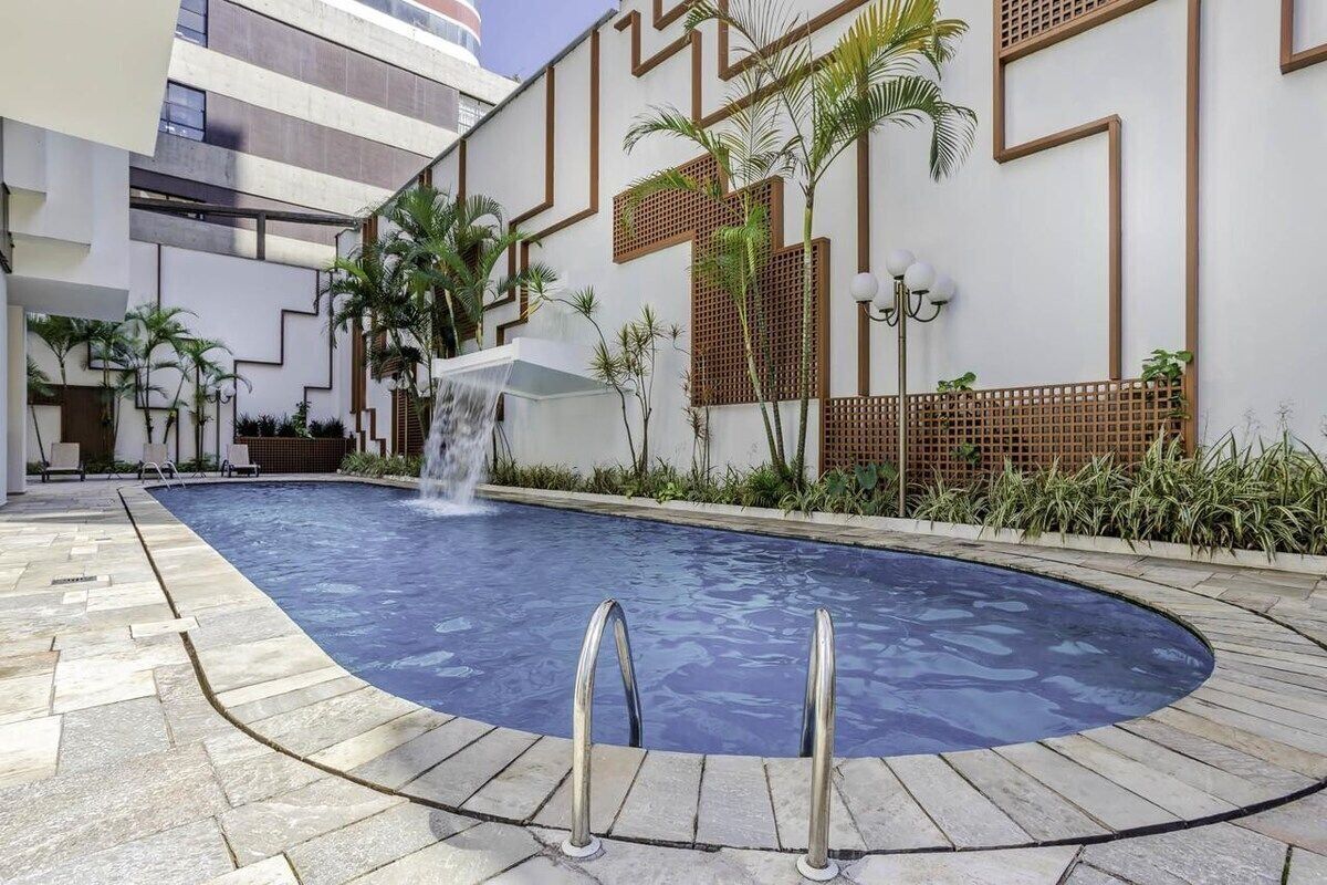 Ein Pool mit Wasserfall, umgeben von einem modernen Gebäude mit geometrischen Wanddesigns und Palmen.